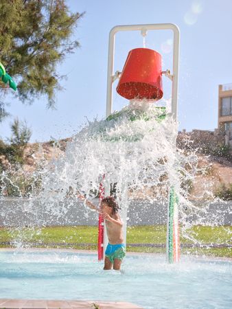 Happy boy playing with splashing waterfall from bucket