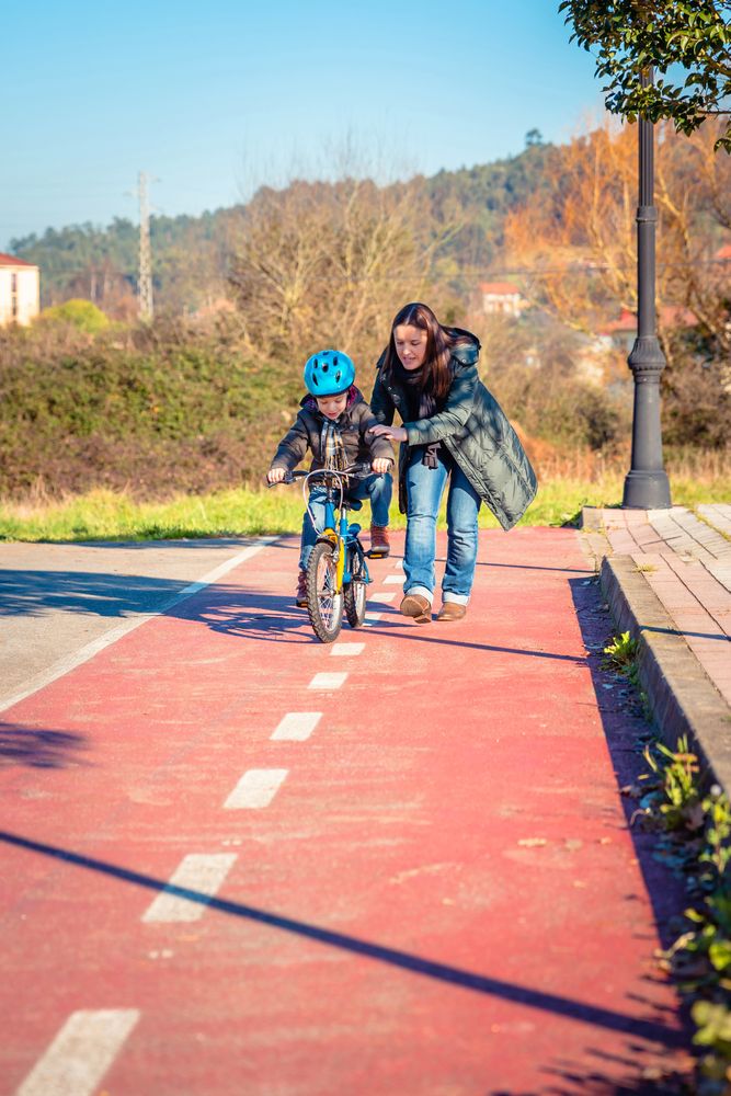 Woman helping boy to ride his bike, vertical