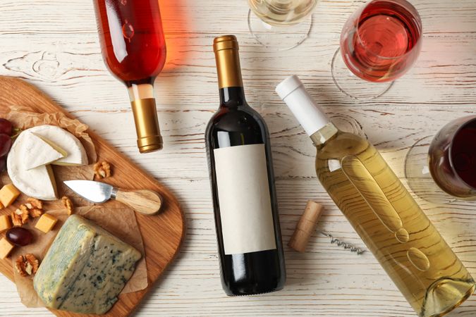 Grape, cheese, bottles and glasses with different wine on light wooden background, top view