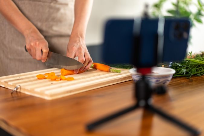 Cooking content creator chopping fresh carrots kitchen smartphone filming healthy food preparation video blog