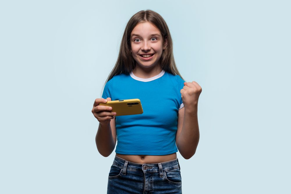Girl raising fist while looking at smartphone, excited and happy.