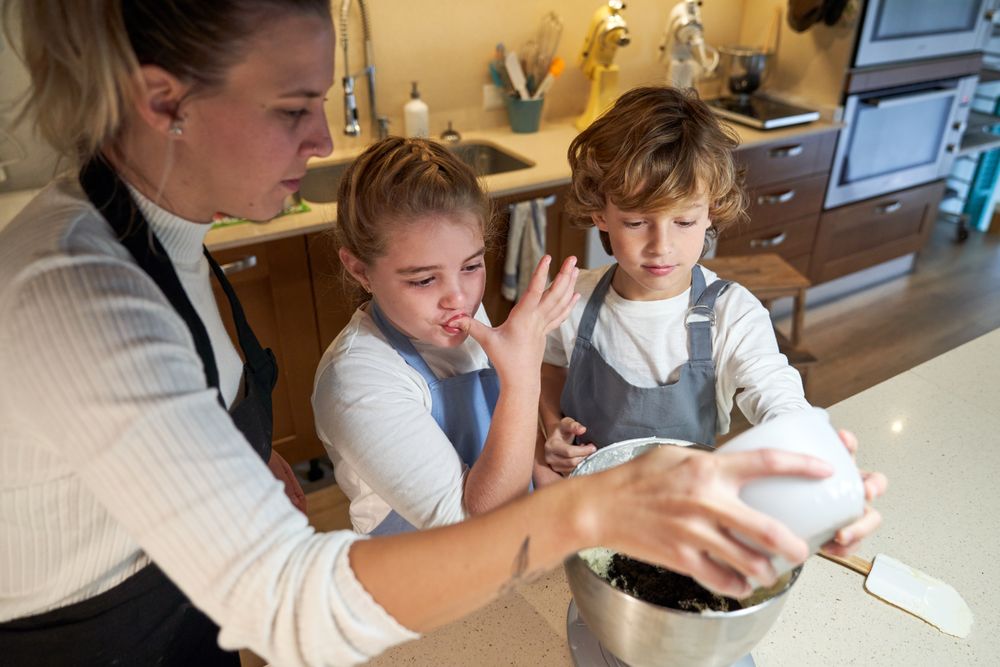 Two boys and a girl with apron in the kitchen mixing ingredients preparing cupcakes