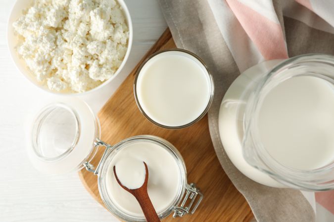 Fresh dairy products, board and towel on plain wooden table, top view