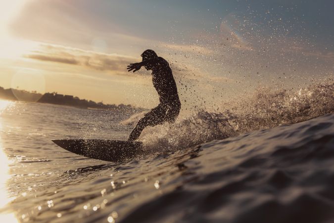 Man on surf board on waving water at sunset