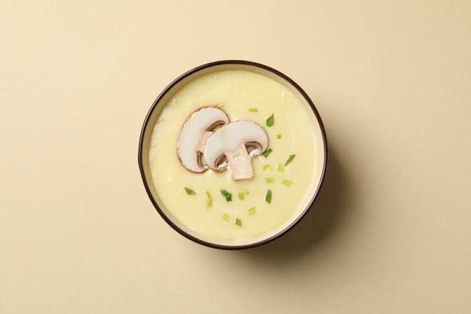 Looking down at bowl of mushroom soup on beige background