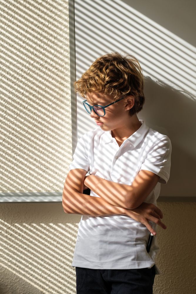 Sad schoolboy standing with crossed arms in classroom