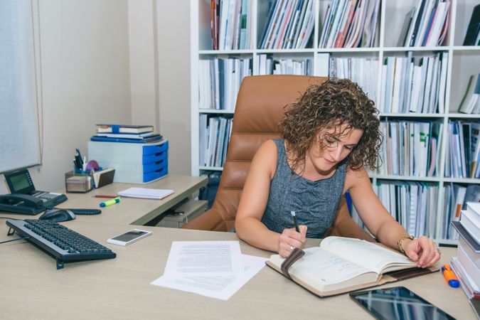 Businesswoman with curly hair writing in notebook in the office