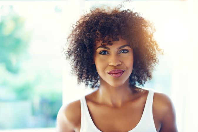 Confident female with curly hair on leafy background, copy space