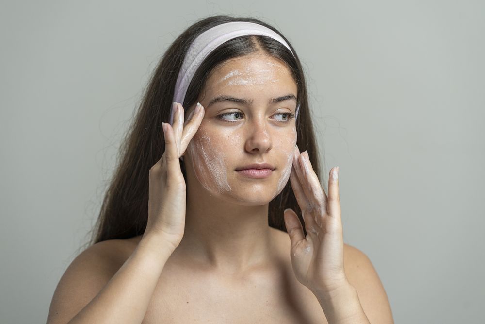 Beautiful woman looking at camera while washing her face with a cleansing scrub or mask