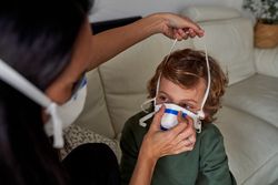 Woman putting on protective mask on face of little kid