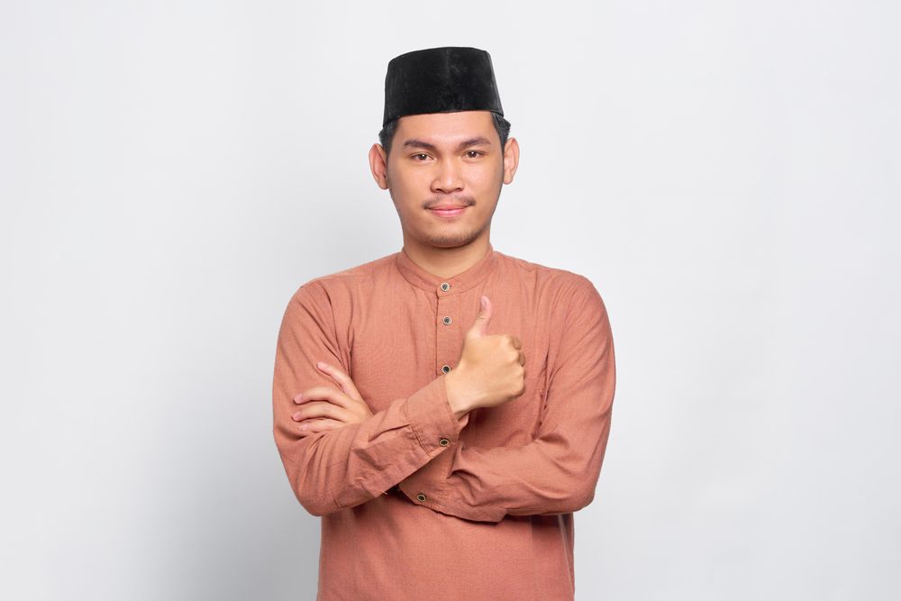 Muslim man in kufi hat making thumbs up gesture with hand