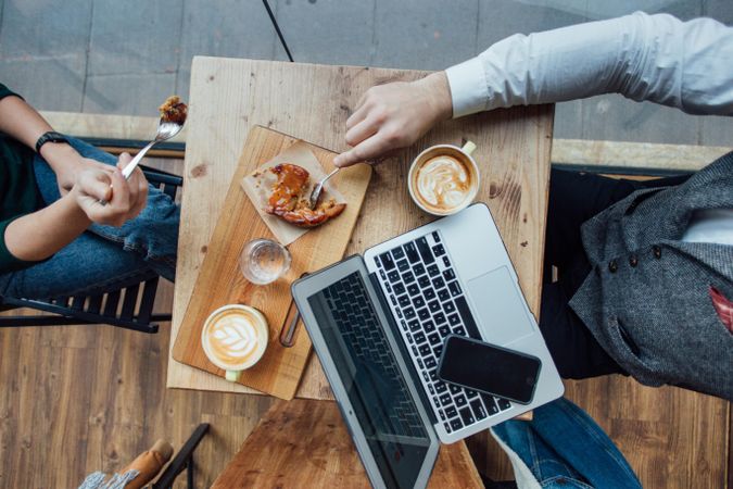 Top view of cafe table with pastry, lattes and laptop