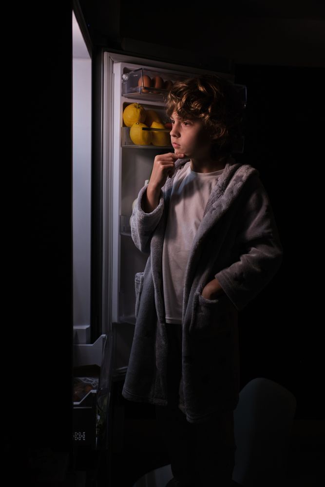 Thoughtful boy near opened refrigerator in dark kitchen