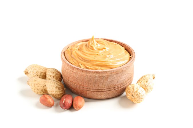 Creamy peanut butter in glass bowl and peanut isolated on bright background. A traditional product of American cuisine
