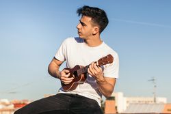 young man sitting playing ukelele on a rooftop