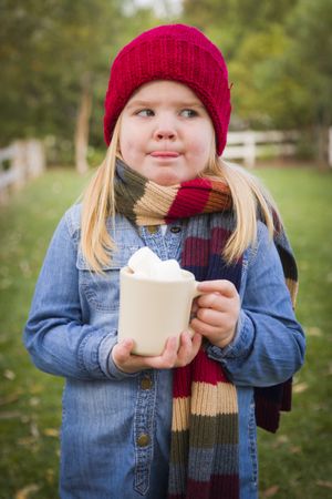 Cute Young Girl Holding Cocoa Mug with Marsh Mallows Outside