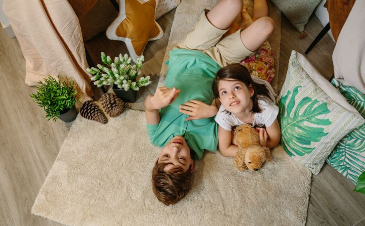 Boy pointing with his finger up and smiling little girl looking while embracing stuffed dog.