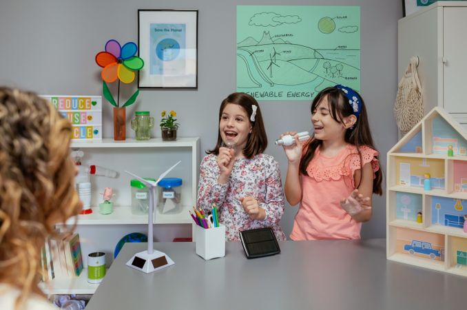 Female students singing using light bulbs as microphones in ecology classroom