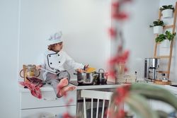 Adorable preteen boy in chef suit reading culinary book