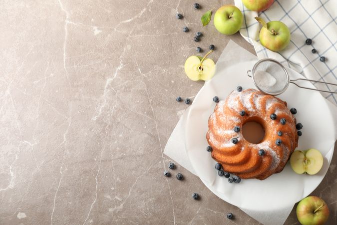 Cake with powder sugar, blueberry and apples on grey background, top view