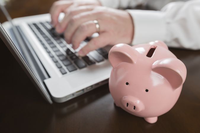 Piggy Bank Near Male Hands Typing on Laptop