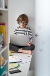 Boy using laptop while sitting on table in bedroom