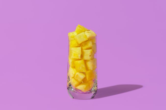 Glass with pineapple cubes isolated on a purple background