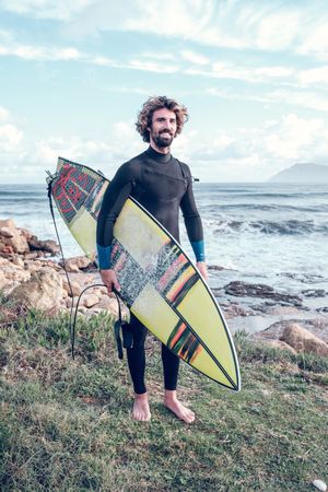 Smiling sportsman standing at seaside with surfboard