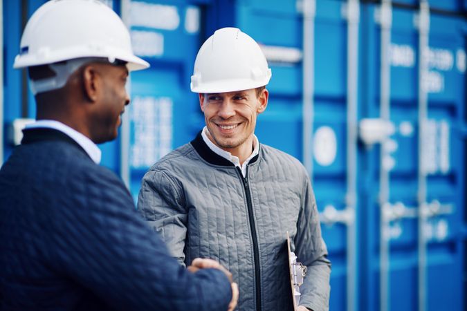 Two men in hard hats smiling and shaking hands