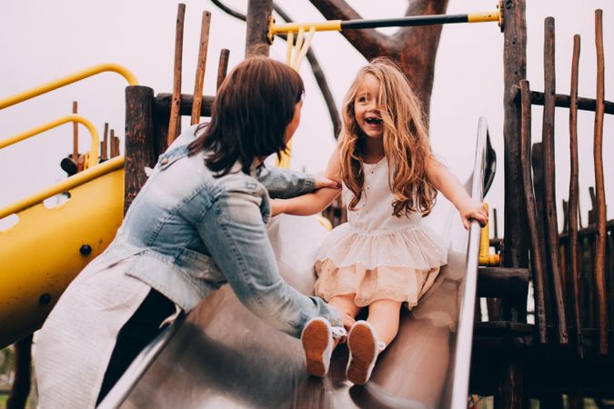 Woman and girl play on a slide of a playground