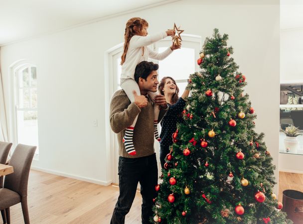 Young girl piggy-backing on father's shoulder put star on top of Christmas tree