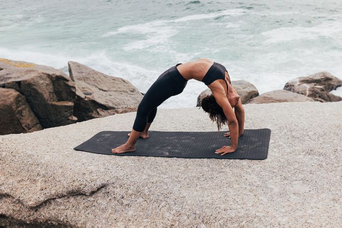 Female stretching her back in bridge pose while next to the ocean