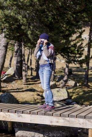 Woman standing on small footbridge in forest with camera