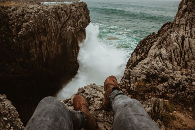 Person sitting on edge of cliff near water