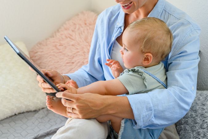 Crop woman sharing tablet with baby