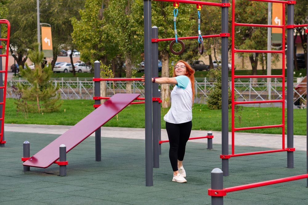 Woman on outdoor playground, smiling during exercise.