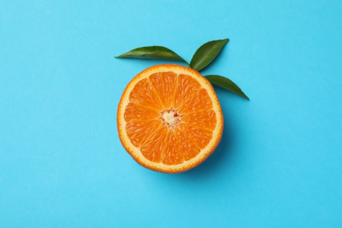 Half of mandarin with leaves on blue background Half of mandarin with leaves on blue background