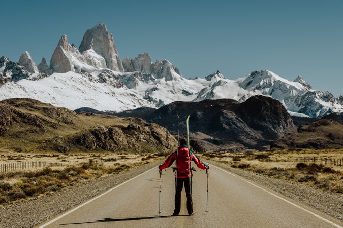 Person with skiing equipment walking on the road toward snowy mountains