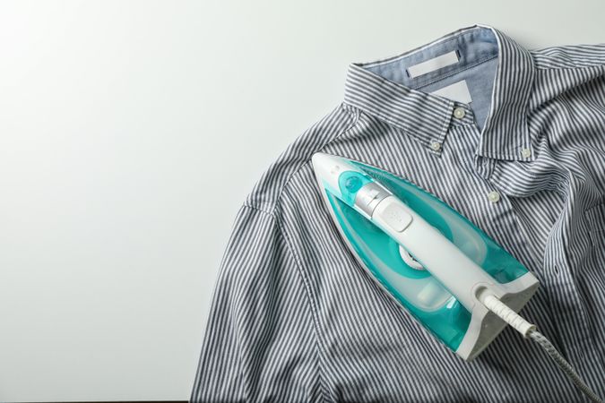 Iron and shirt on blank background, top view