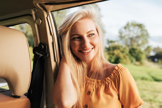 Blonde woman leaning on a van door with her hand in her hair