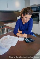 Woman calculating her monthly bills in her kitchen bGaoY5