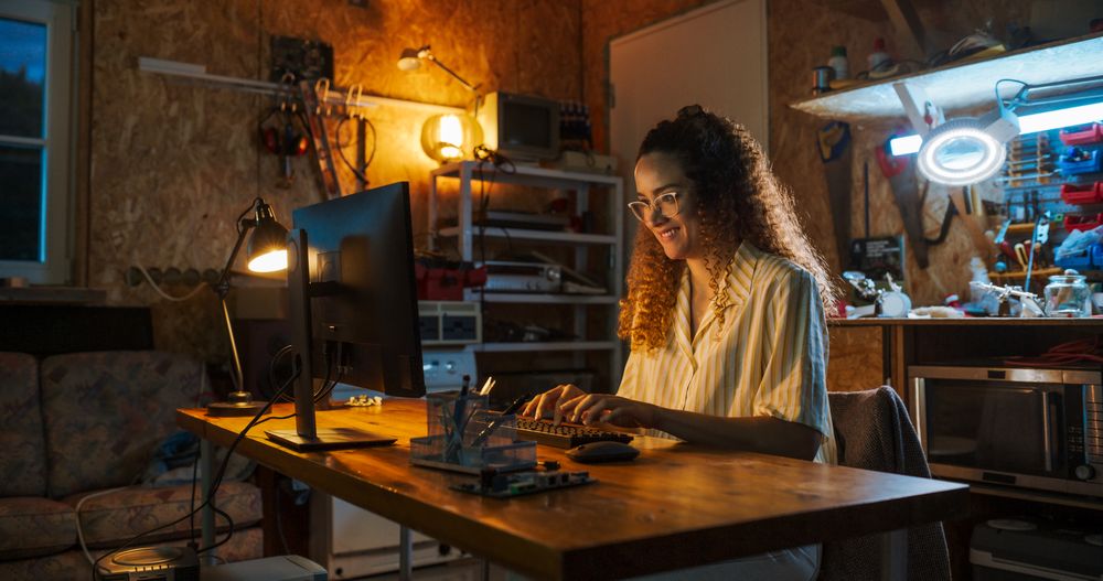 Portrait of Hispanic Female Software Engineer Programming on Desktop Computer In Retro Garage Late At Night.