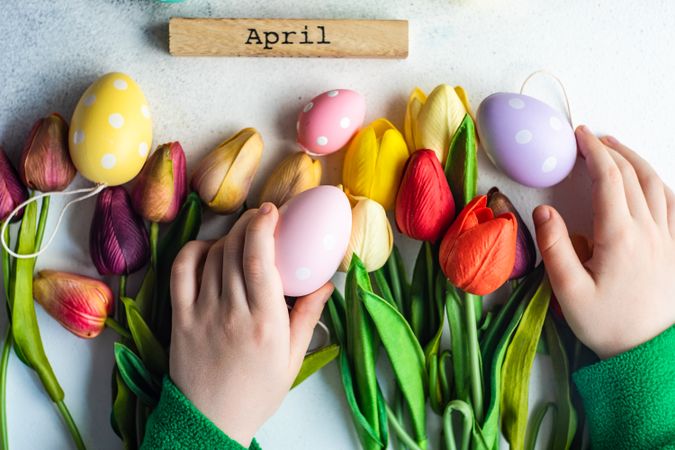 Flat lay of hands reaching for tulips and egg decorations