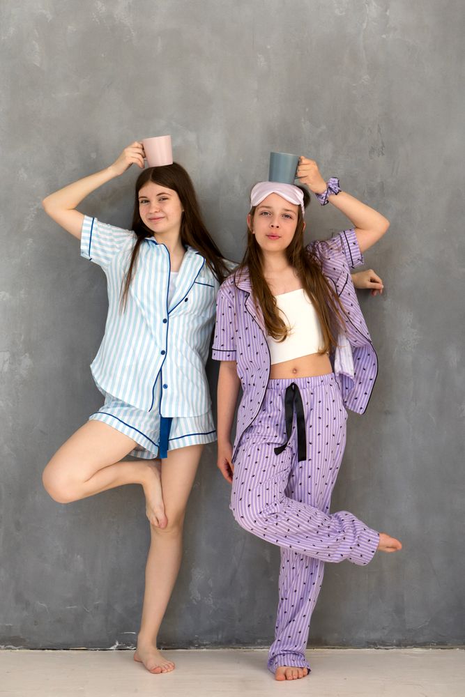 Young girls in pajamas balancing cups on heads, smiling.