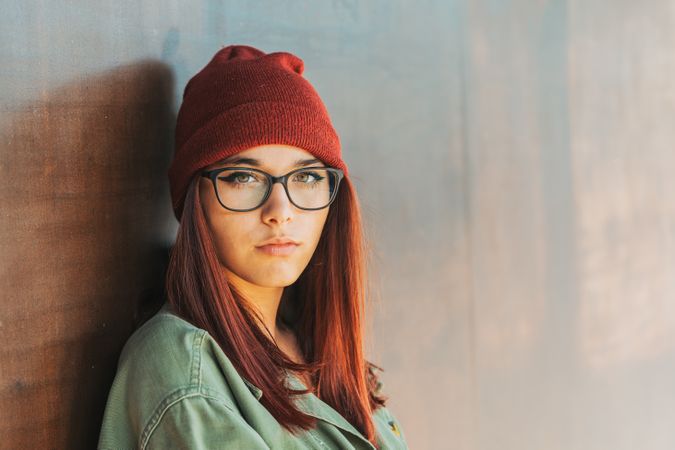 Woman in glass and hat leaning on wall