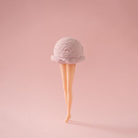 Doll legs with ice cream scoop on pastel pink background