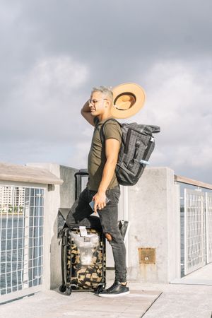 Full length portrait of a tourist taking out his hat, with suitcase and a backpack