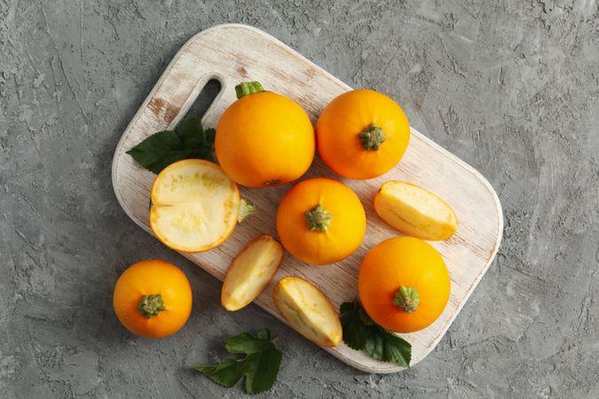 Board with round zucchini and leaves on gray background