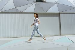Cheerful woman jumping near modern wall