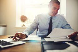 Man in business attire working at his laptop with documents in hand